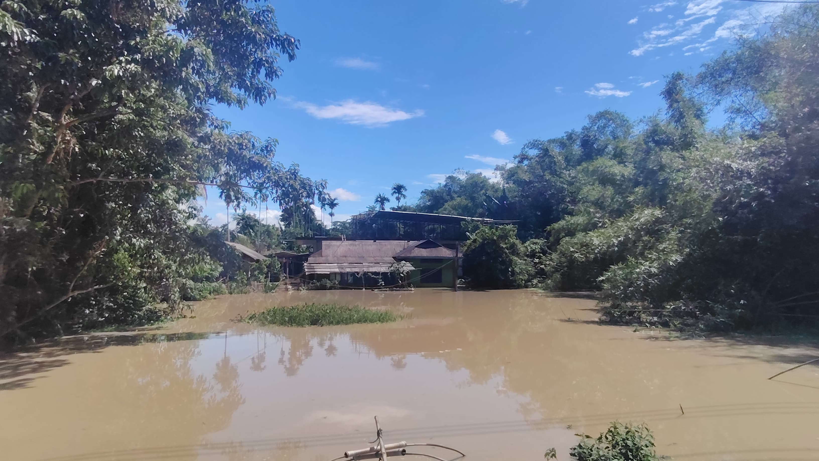 A submerged homestead seen across a wide expanse of floodwater under clear sky