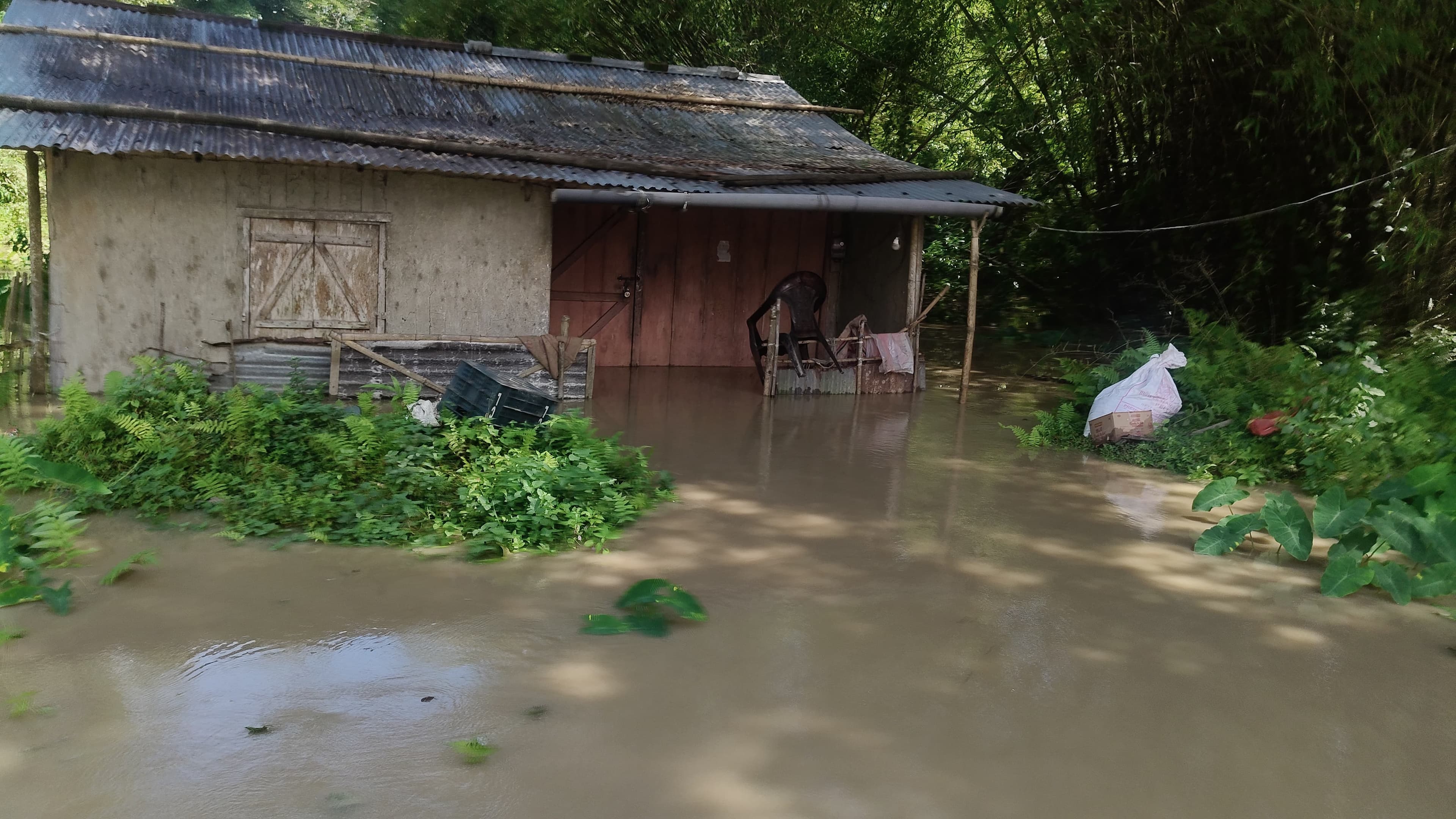 Floodwater standing at door height inside a village home, its veranda furniture half submerged