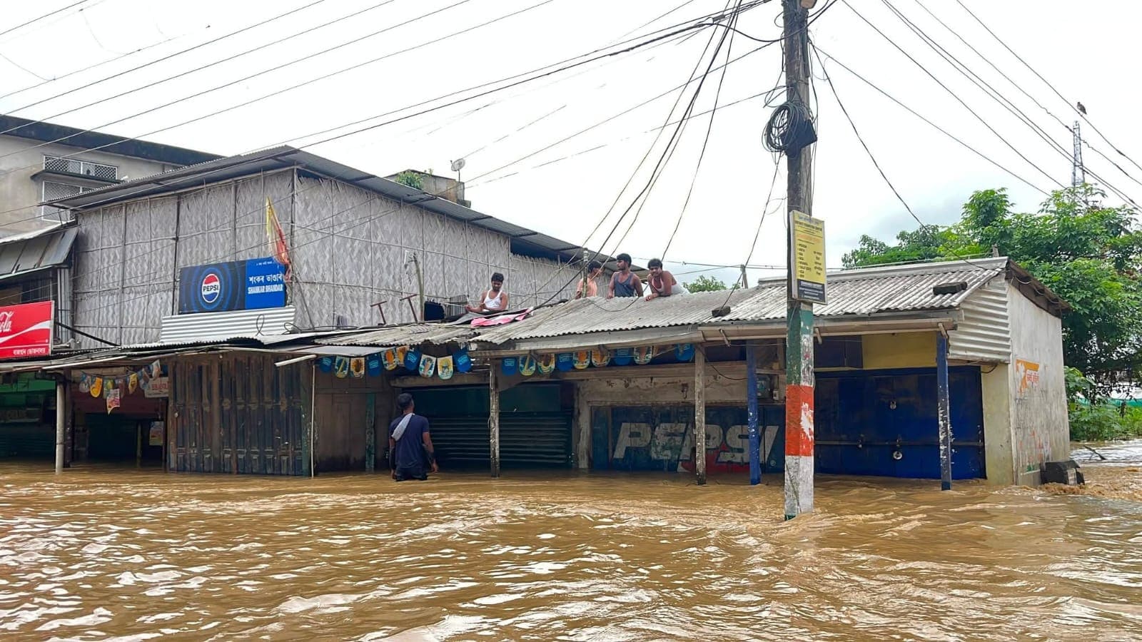 Residents wait on the tin roof of a flooded market row as brown water surges through the street below